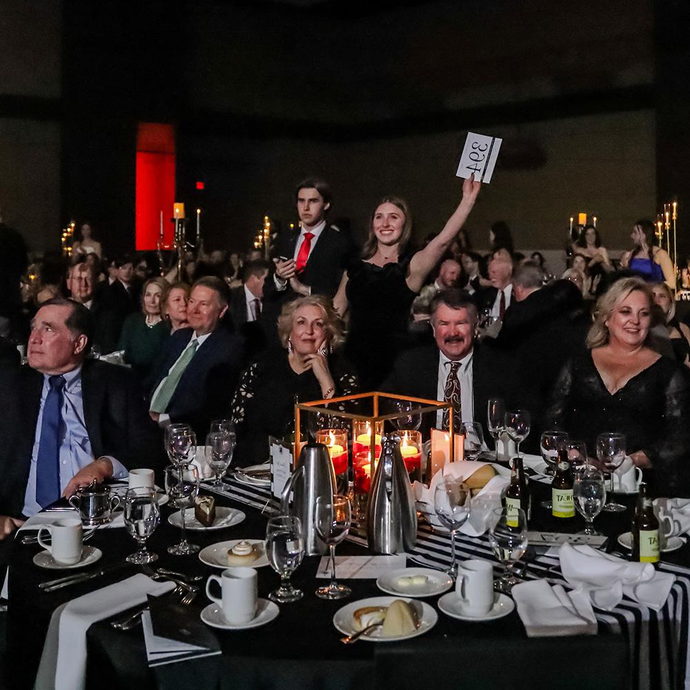 A student hostess raises a bid card for a donor at the Scholarship Ball